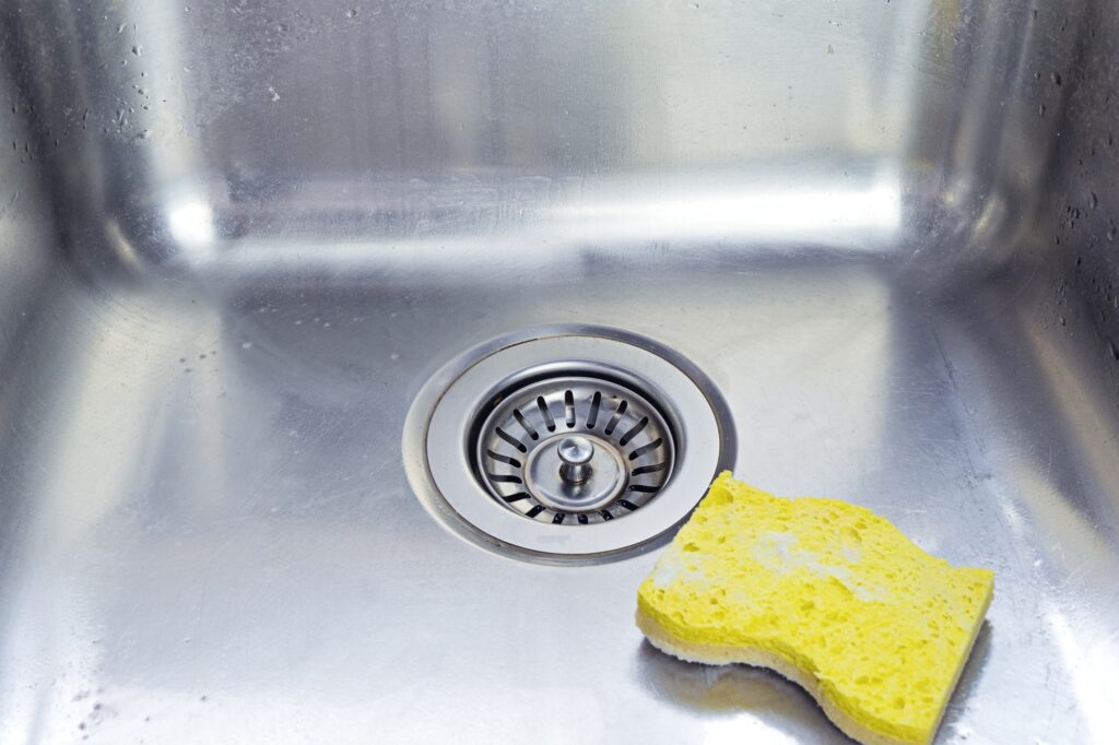 Cleaning polished stainless shiny sink with scrub sponge in kitchen, above view